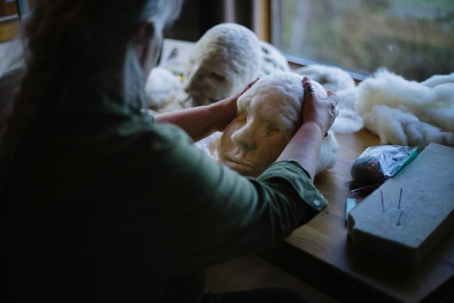 Artist Rosemarie Péloquin needle-felting a 3D face with white natural wool; sitting at a table in improvised studio at Falcon Trails Resort residency. photo: Emily Christie