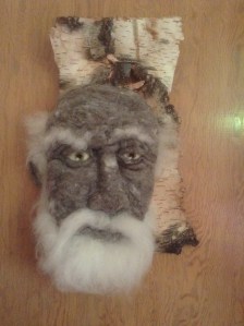 Marcus - Hand needle-felted wool sculpture of a male face with green eyes and wispy white beard and eyebrows. Mounted on reclaimed birch bark. Artist/photo: Rosemarie Péloquin.