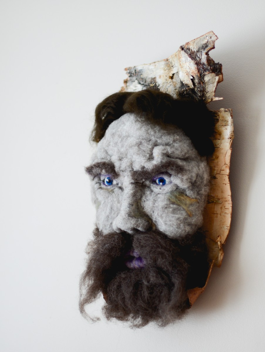 Ti-Jean - Hand needle-felted wool sculpture of a male face – dark brown hair, moustache and beard. Mounted on reclaimed birch bark. Artist: Rosemarie Péloquin; photo: Emily Christie.