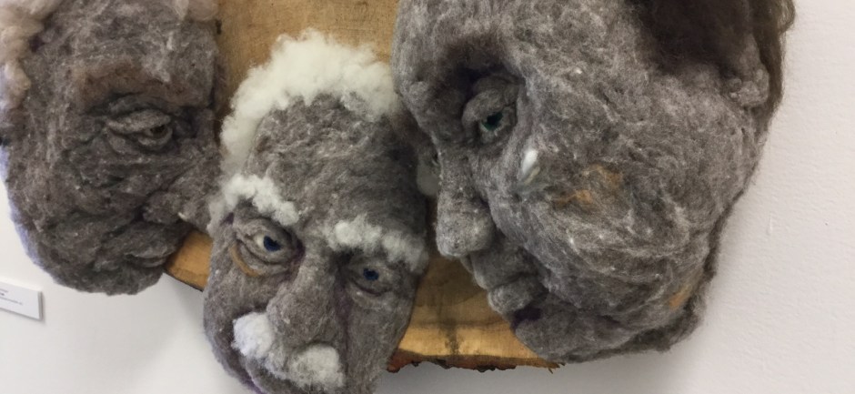 The Meeting - Hand needle-felted wool sculpture of three male faces leaning together, seeming to whisper. Mounted on cottonwood slice. artist: Rosemarie Péloquin; photo: Anne Fallis