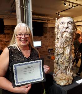 Rosemarie Péloquin standing with her certificate beside her winning sculpture.